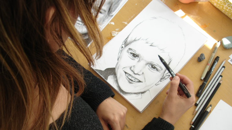 Pige tegner portræt af dreng med blyant